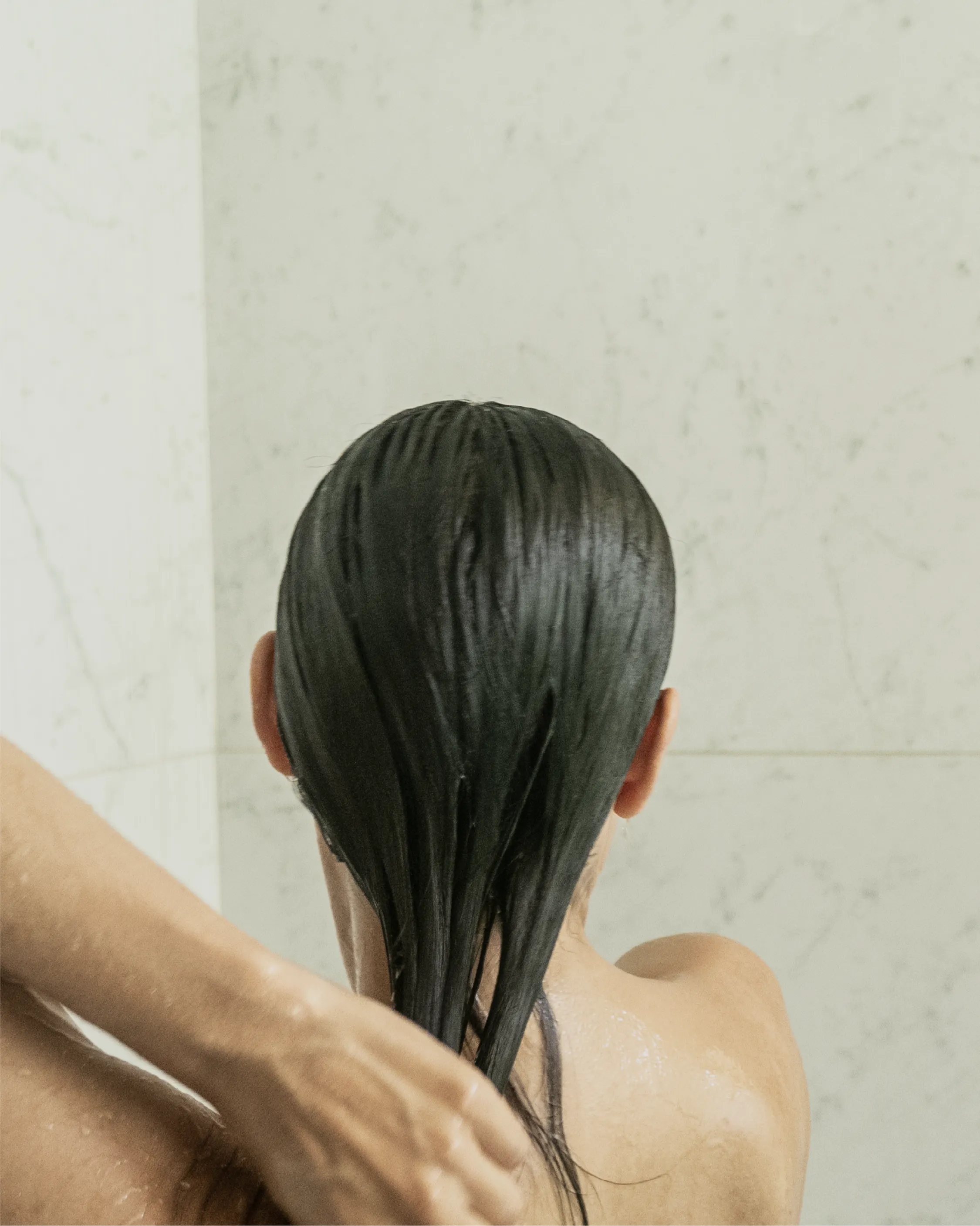 Back view of a person rinsing Blu & Green Daily Conditioner Concentrate from hair in the shower.