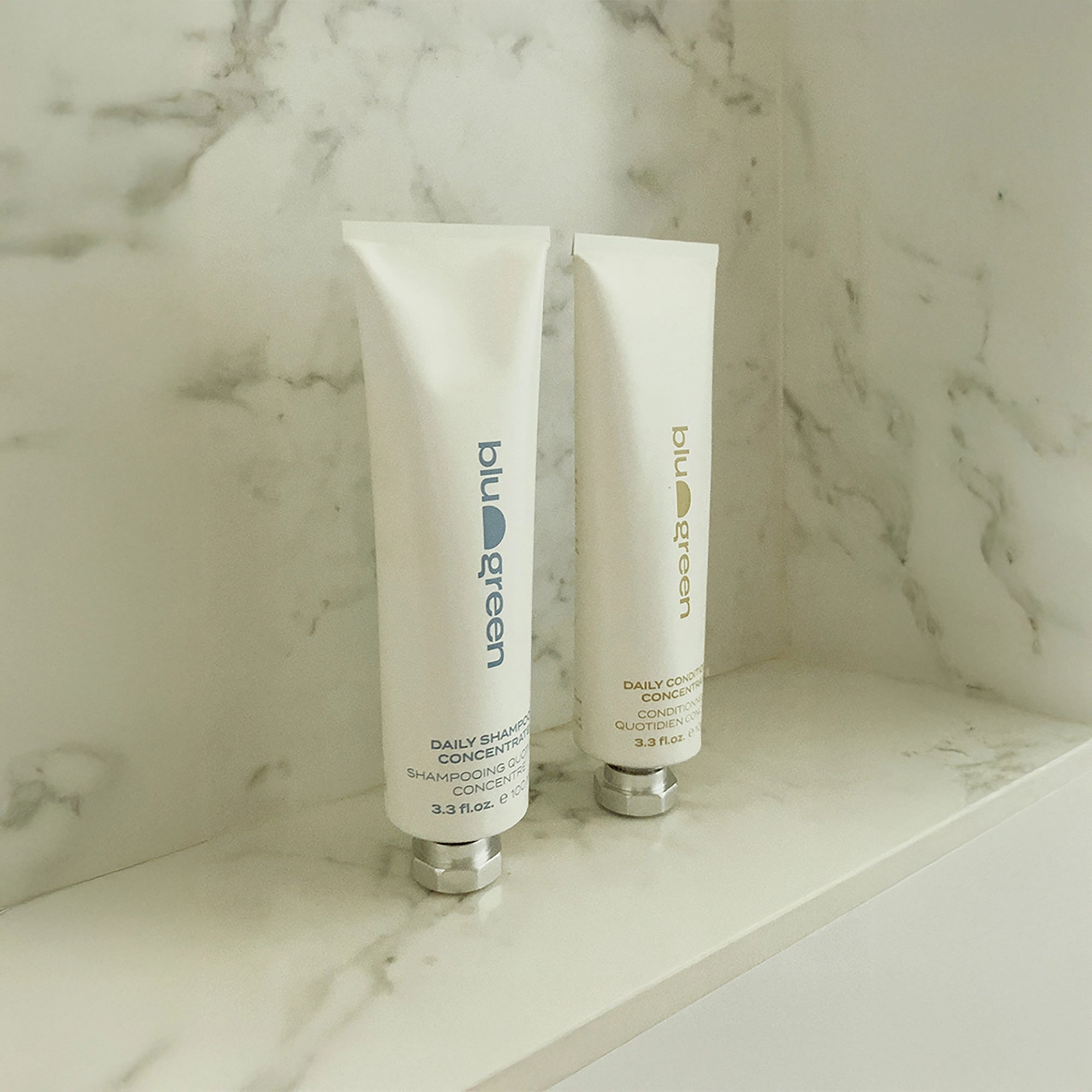 Blu & Green Daily Shampoo Concentrate and Daily Conditioner Concentrate standing on a marble shelf in the shower.
