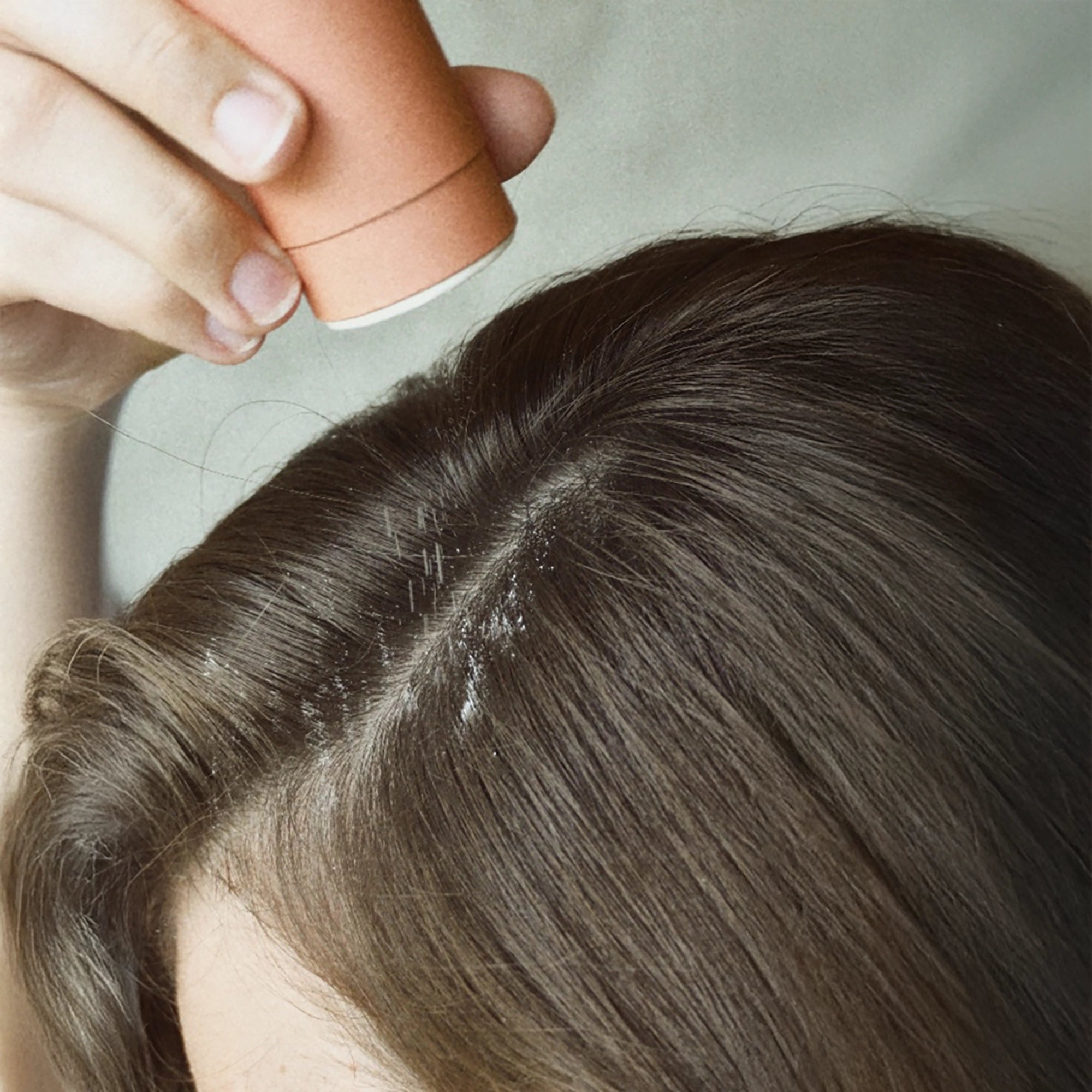 Close-up of Blu & Green dry shampoo being applied to the roots of brown hair.