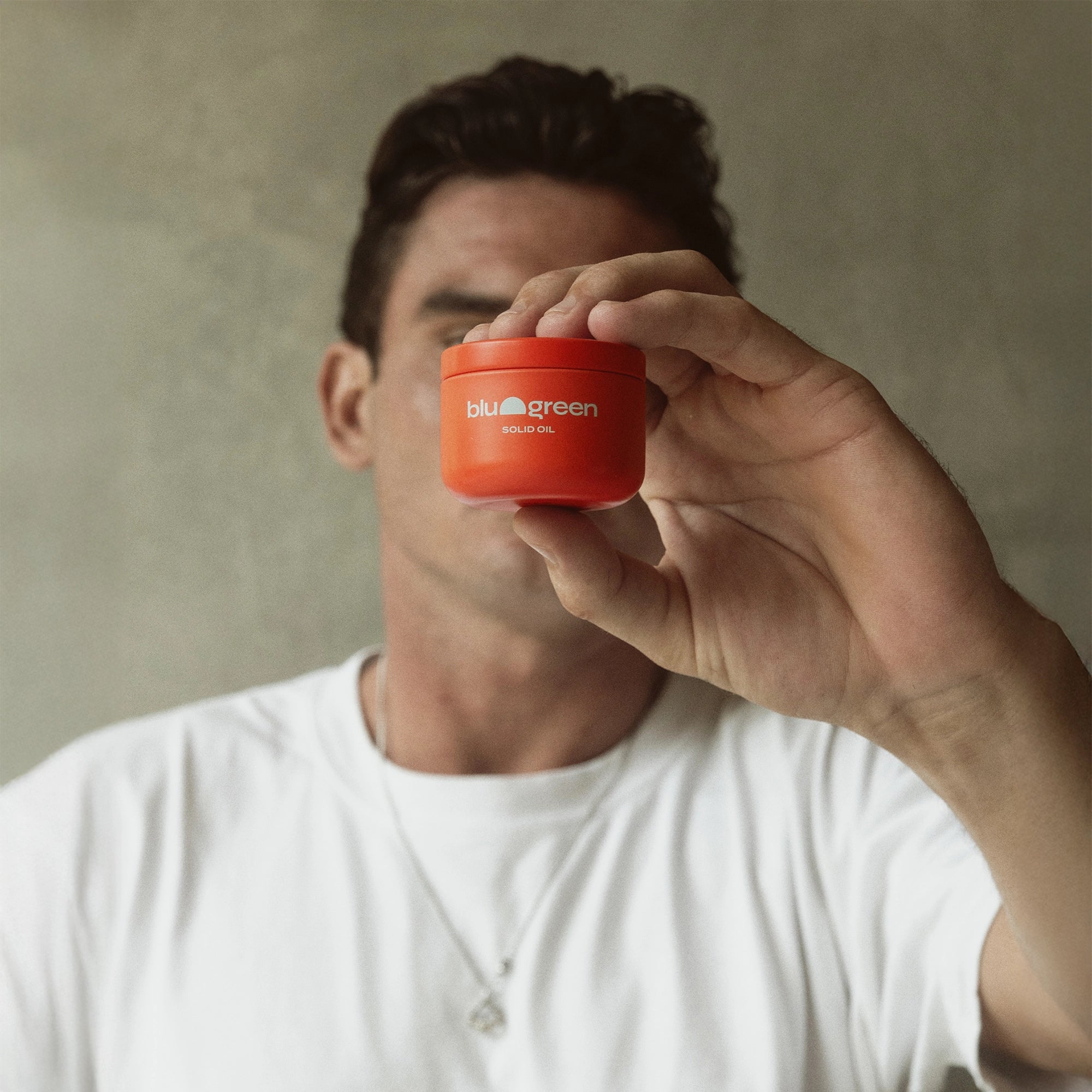 Man holding a Blu & Green Solid Oil container in front of his face.