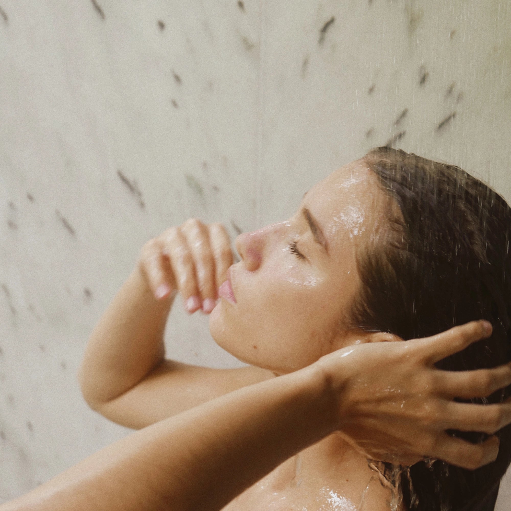 Woman rinsing her hair under running water after conditioning.