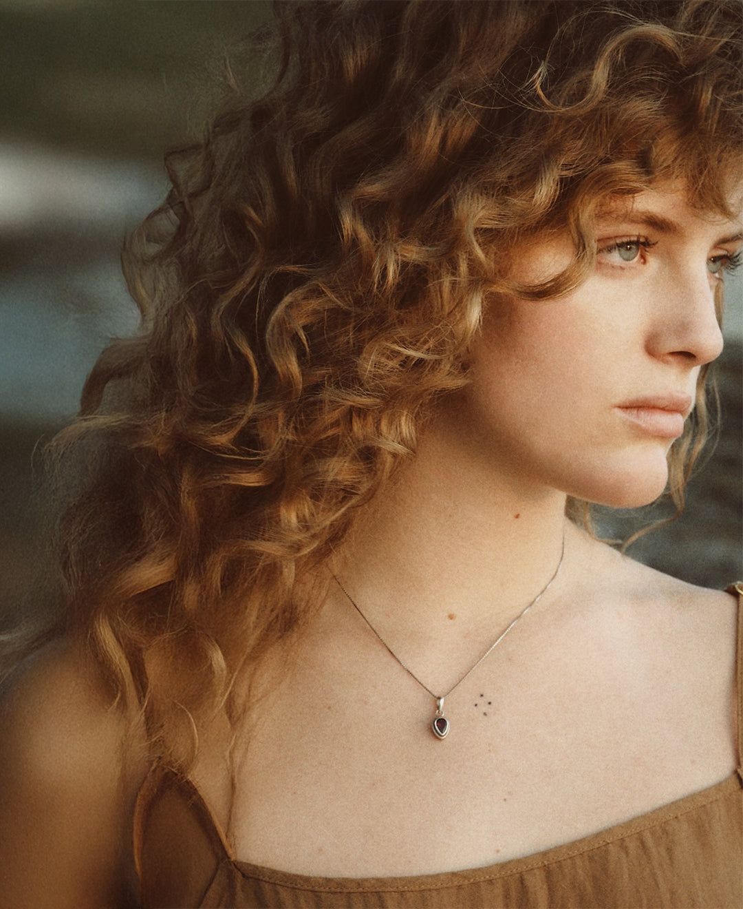 Side profile portrait of a woman with long, curly hair looking to the side.