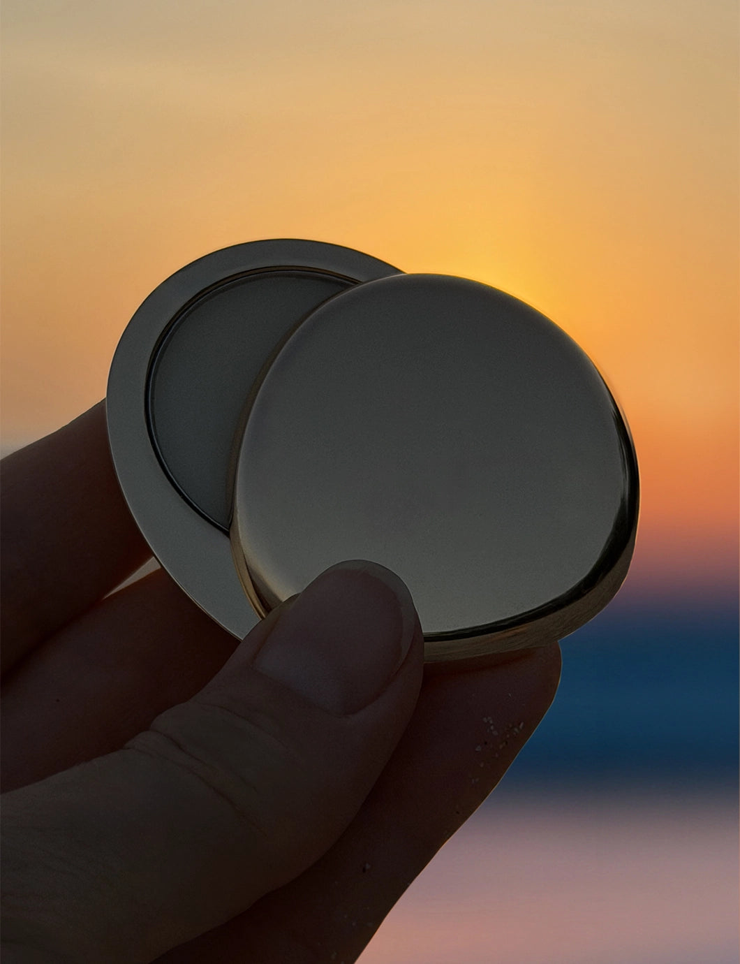 Close-up of Blu & Green's Juniper Dawn Solid Scent, case slightly open, being held in front of a colorful sunrise.