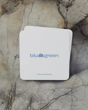 Load image into Gallery viewer, blu and green daily shampoo tablets in flat square off-white tin with a medium blue logo, multiple tins stacked on pale grey dry rocks, diffused sunlight.