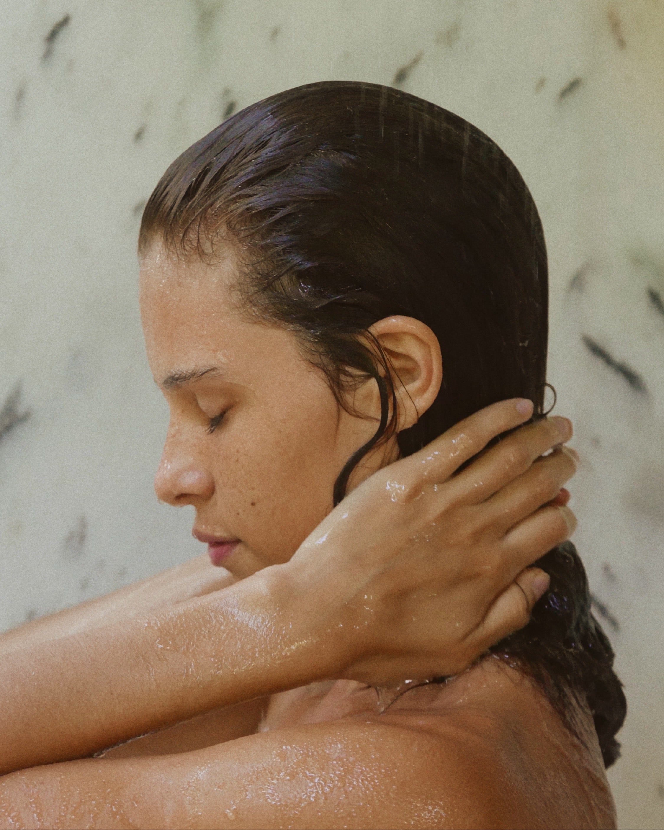 Side profile of woman in shower rising Blu & Green's Weekly Repair Mask out of her hair.