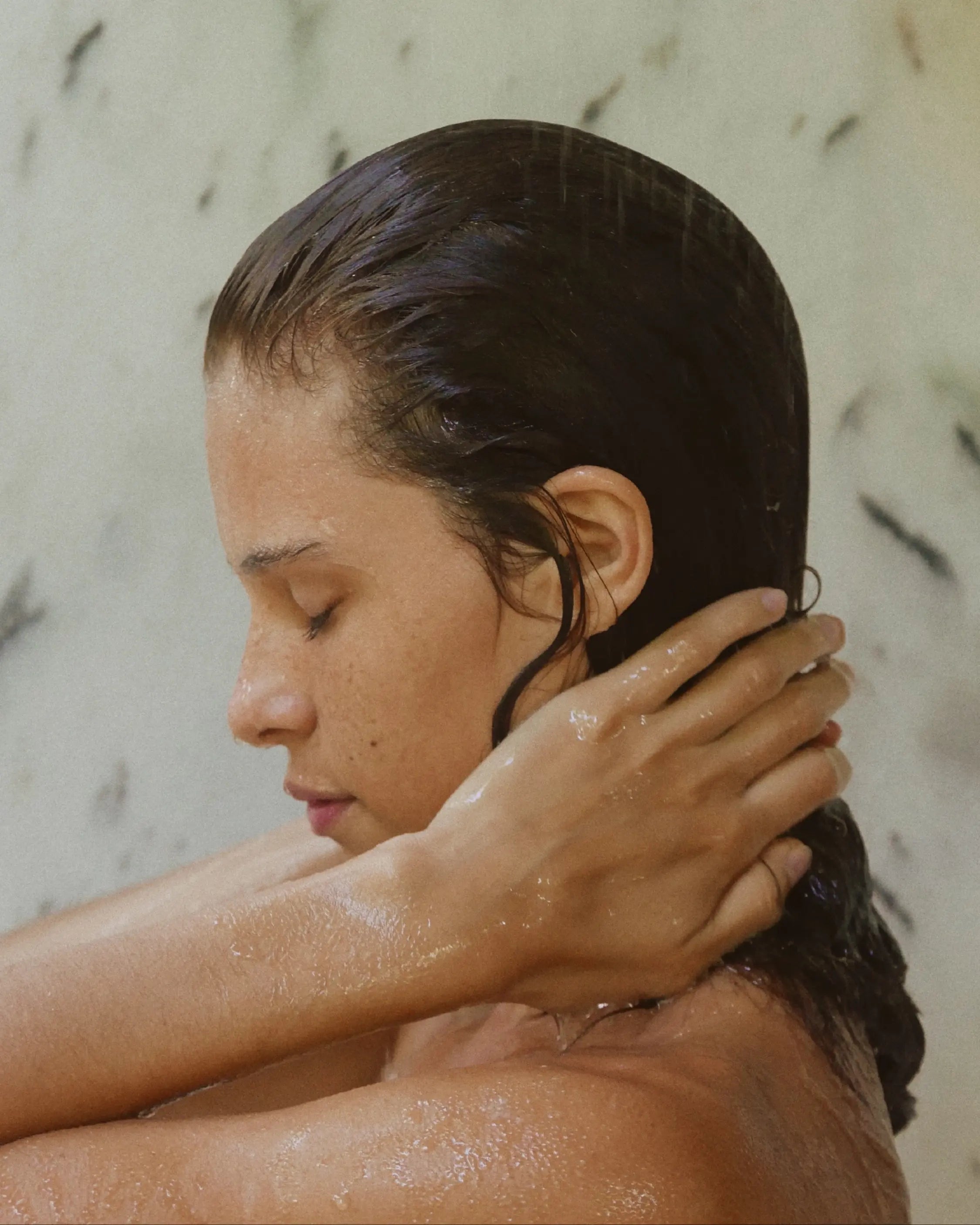 Side profile of woman in shower rising Blu & Green's Weekly Repair Mask out of her hair.
