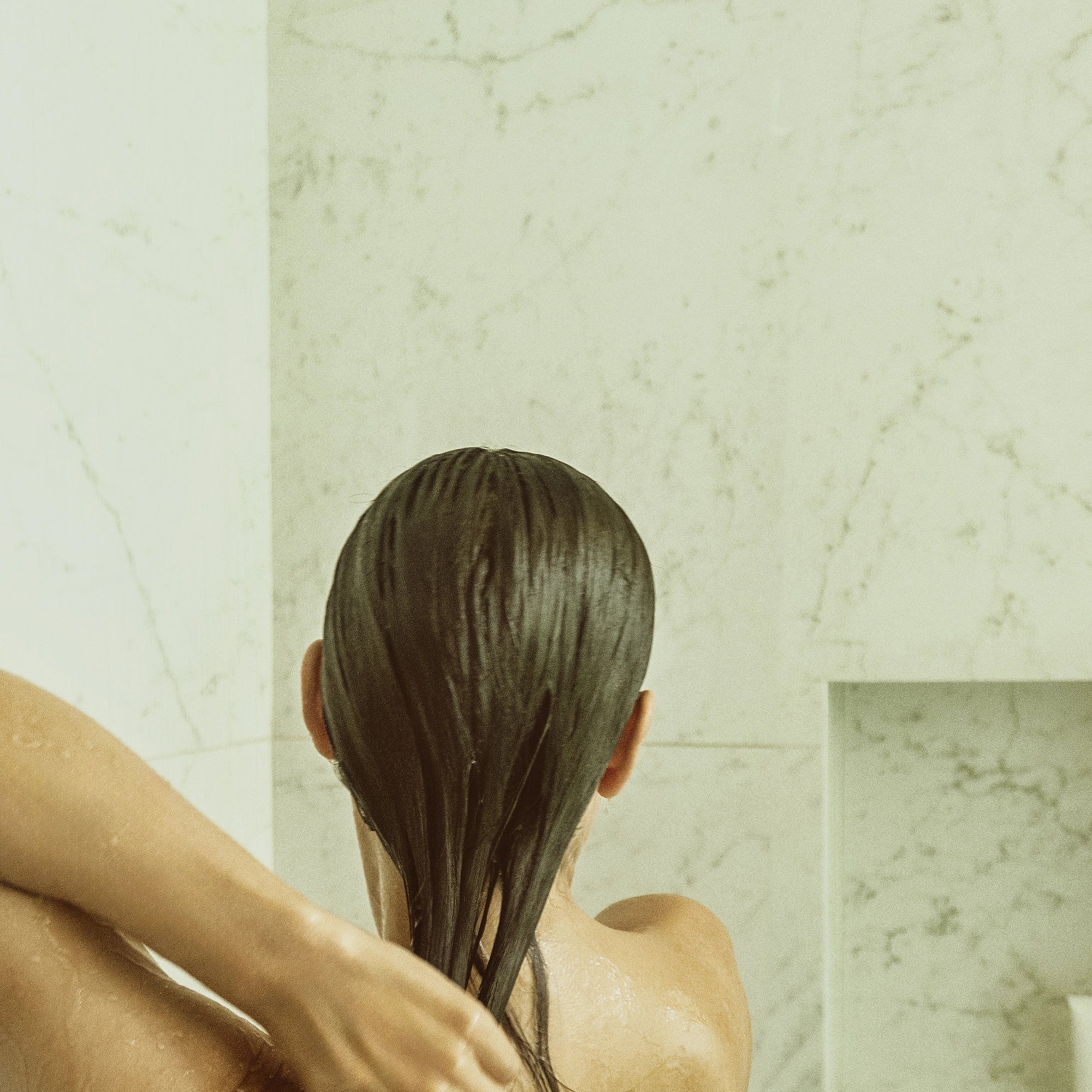 Back view of a person applying Blu & Green Conditioner Concentrate to wet hair in the shower.