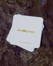 Load image into Gallery viewer, blu and green daily conditioner tablets off-white tin with a pale mustard green colored logo, multiple tins stacked on dark wet rocks, diffused sunlight.