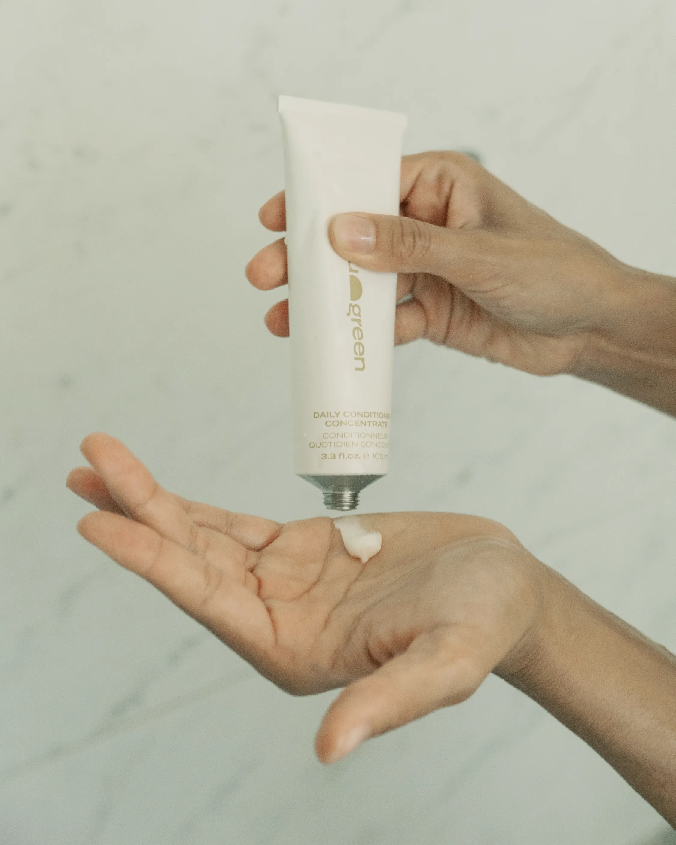 Blu & Green Daily Conditioner Concentrate being squeezed into palm in shower, showcasing the creamy texture.