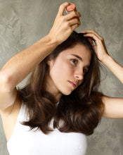 Load image into Gallery viewer, Young brunette woman tapping Blu & Green aerosol-free Dry Shampoo powder onto her roots in front of a neutral background.