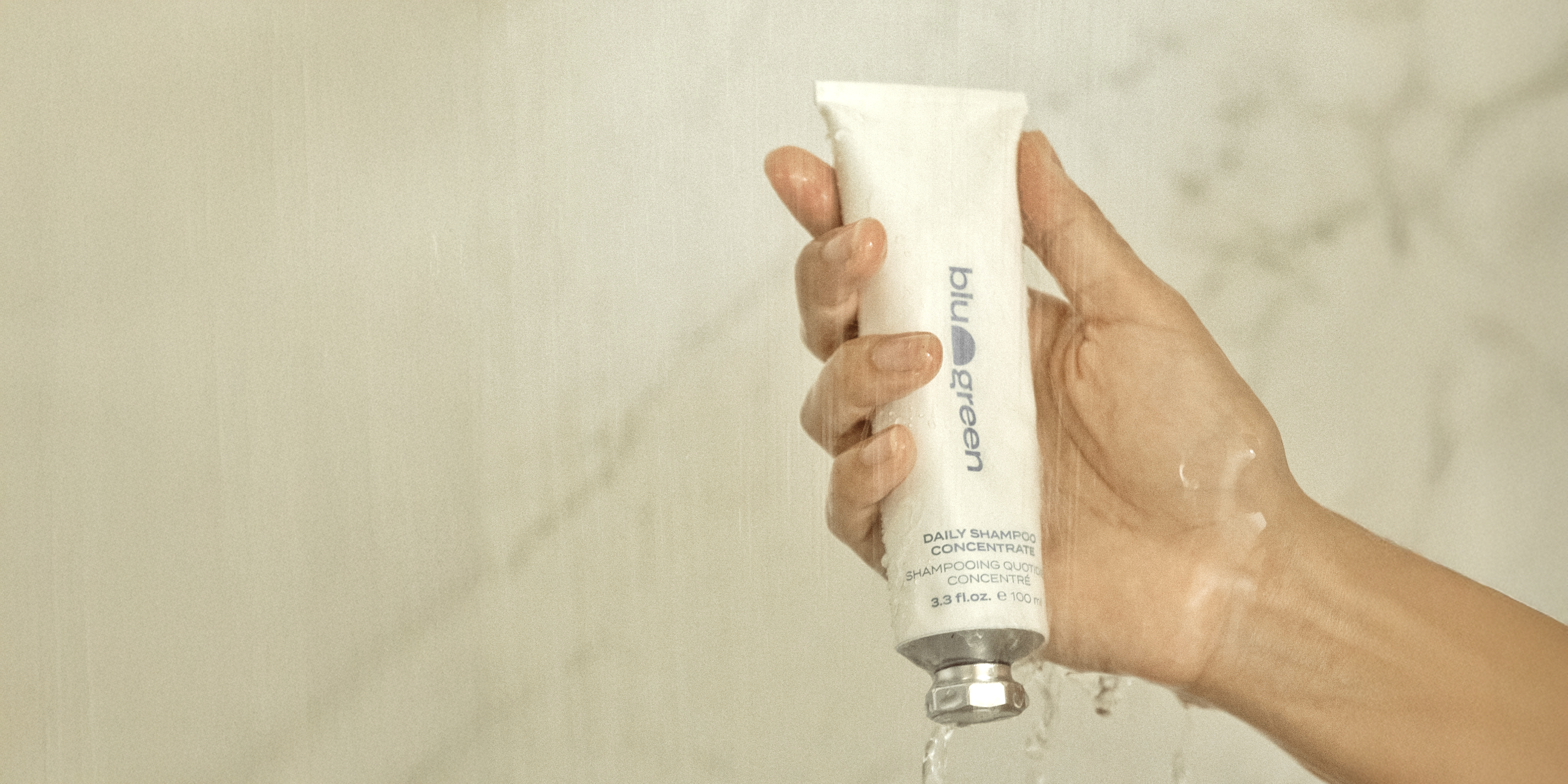 Hand holding Blu & Green Daily Shampoo Concentrate in the shower.