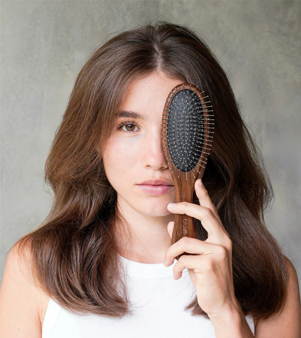 Woman holding Blu & Green's sustainable Walnut Detangling Brush in front of her eye.