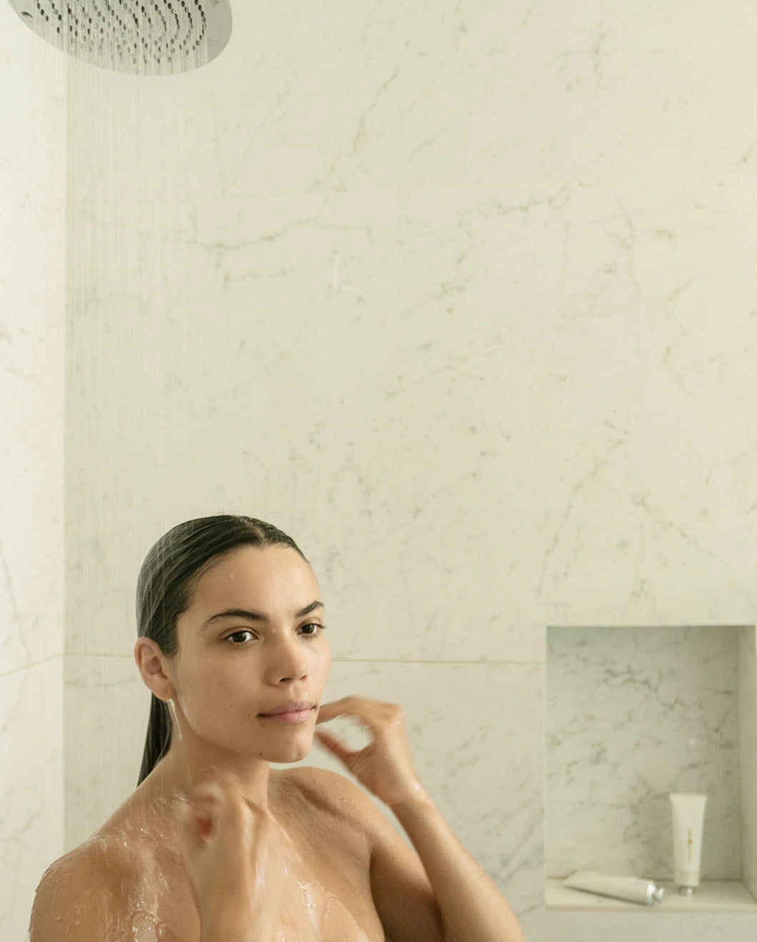 Woman standing in the shower with wet hair, water running over her, with Blu & Green Shampoo & Conditioner Concentrates in the background.