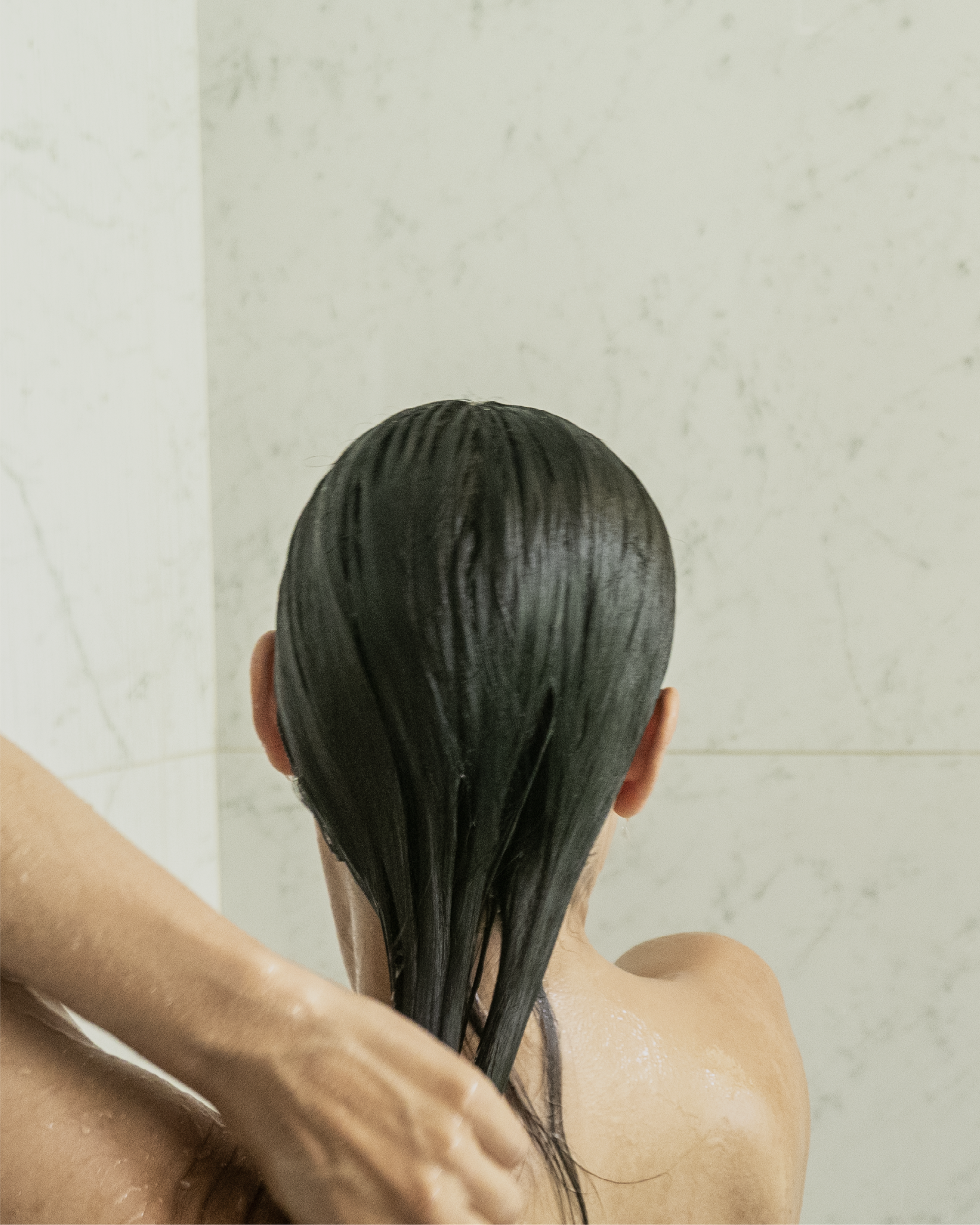 Back view of a person rinsing Blu & Green Daily Conditioner Concentrate from hair in the shower.
