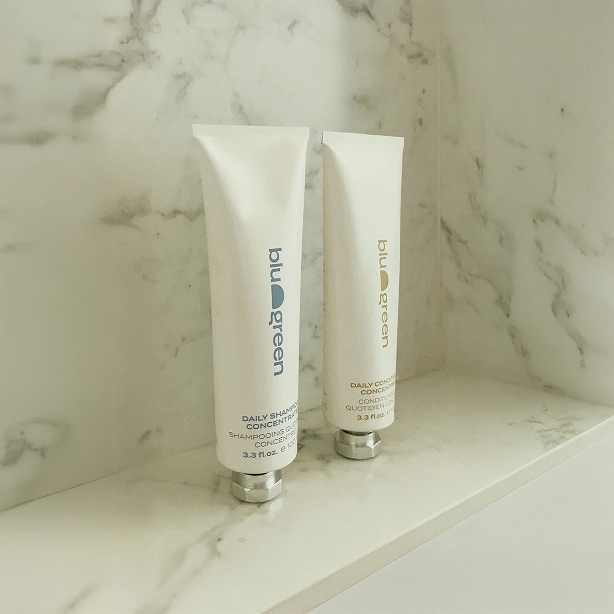 Blu & Green Daily Shampoo Concentrate and Daily Conditioner Concentrate standing on a marble shelf in the shower.
