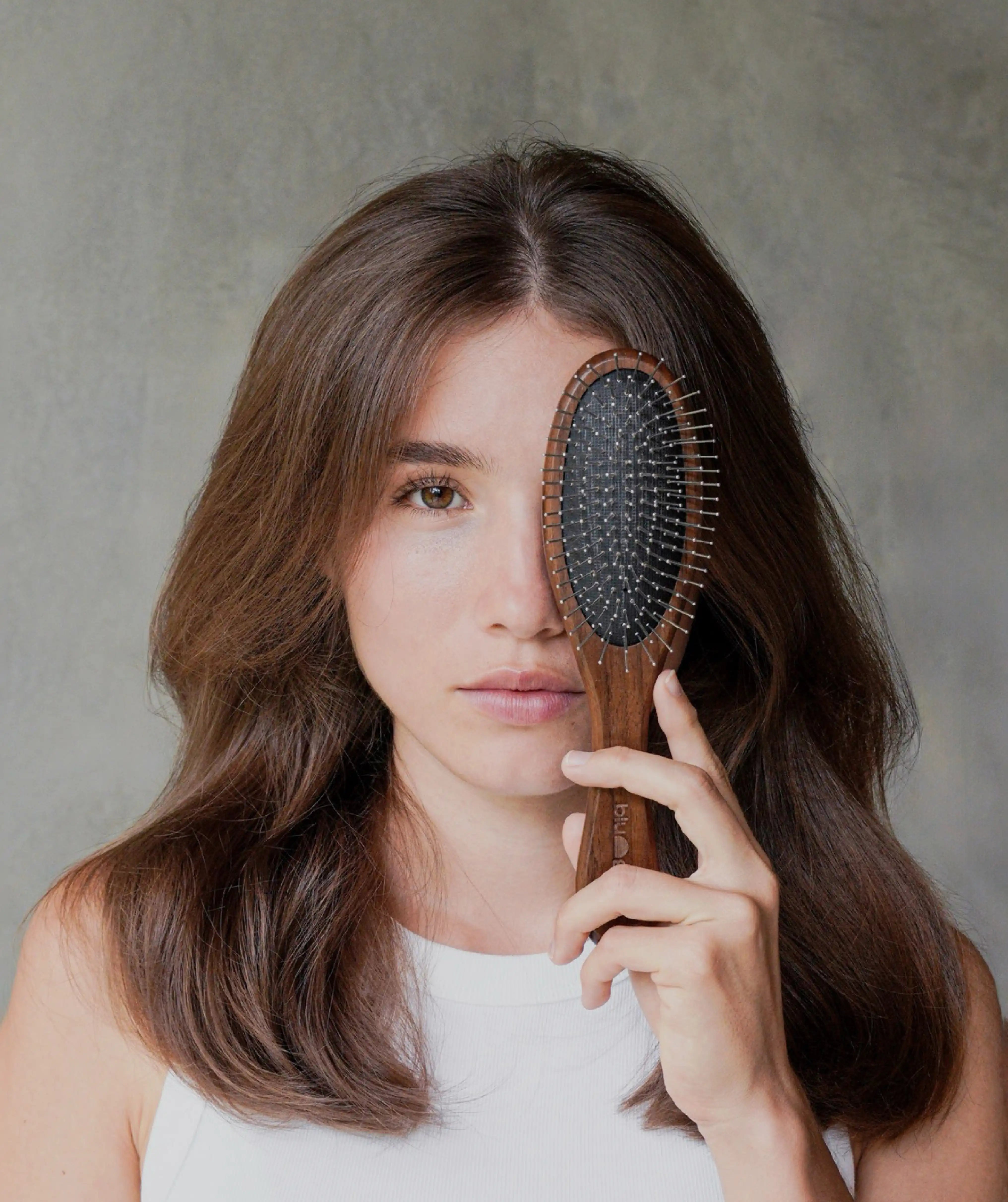 Brunette woman looking into the camera, with the Walnut Detangling Brush covering one of her eyes.