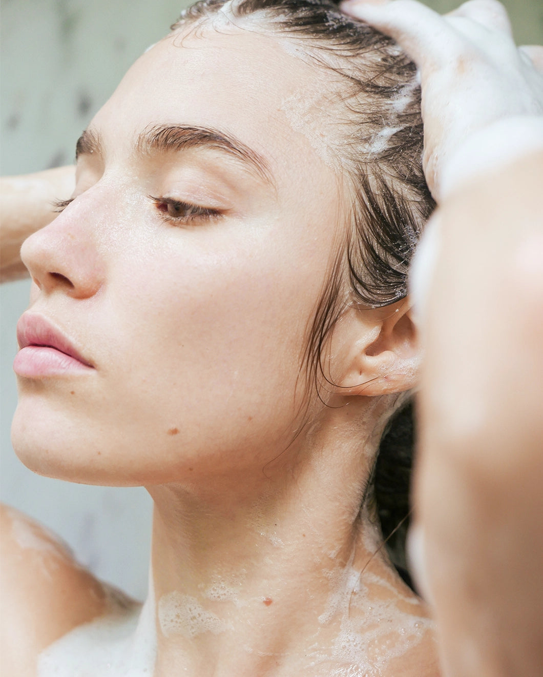 Close-up of a woman washing her hair in the shower with visible lather from Blu & Green shampoo.