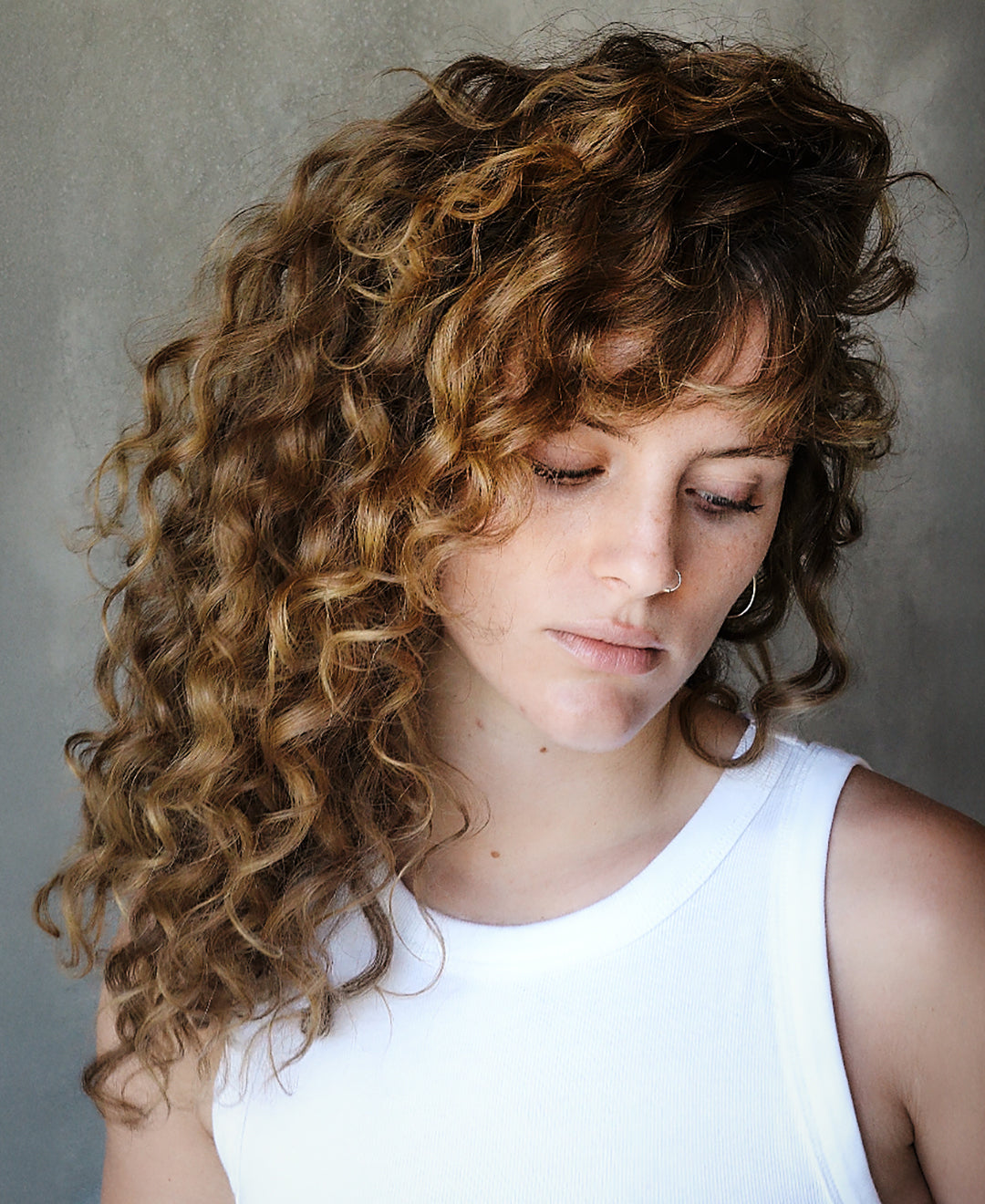 Portrait of a woman with long, curly hair looking downward.