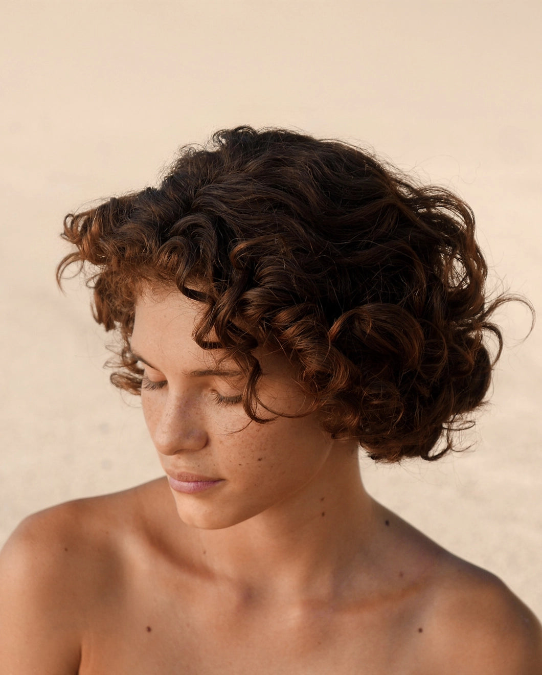Portrait of a woman with short, curly brown hair looking downward.