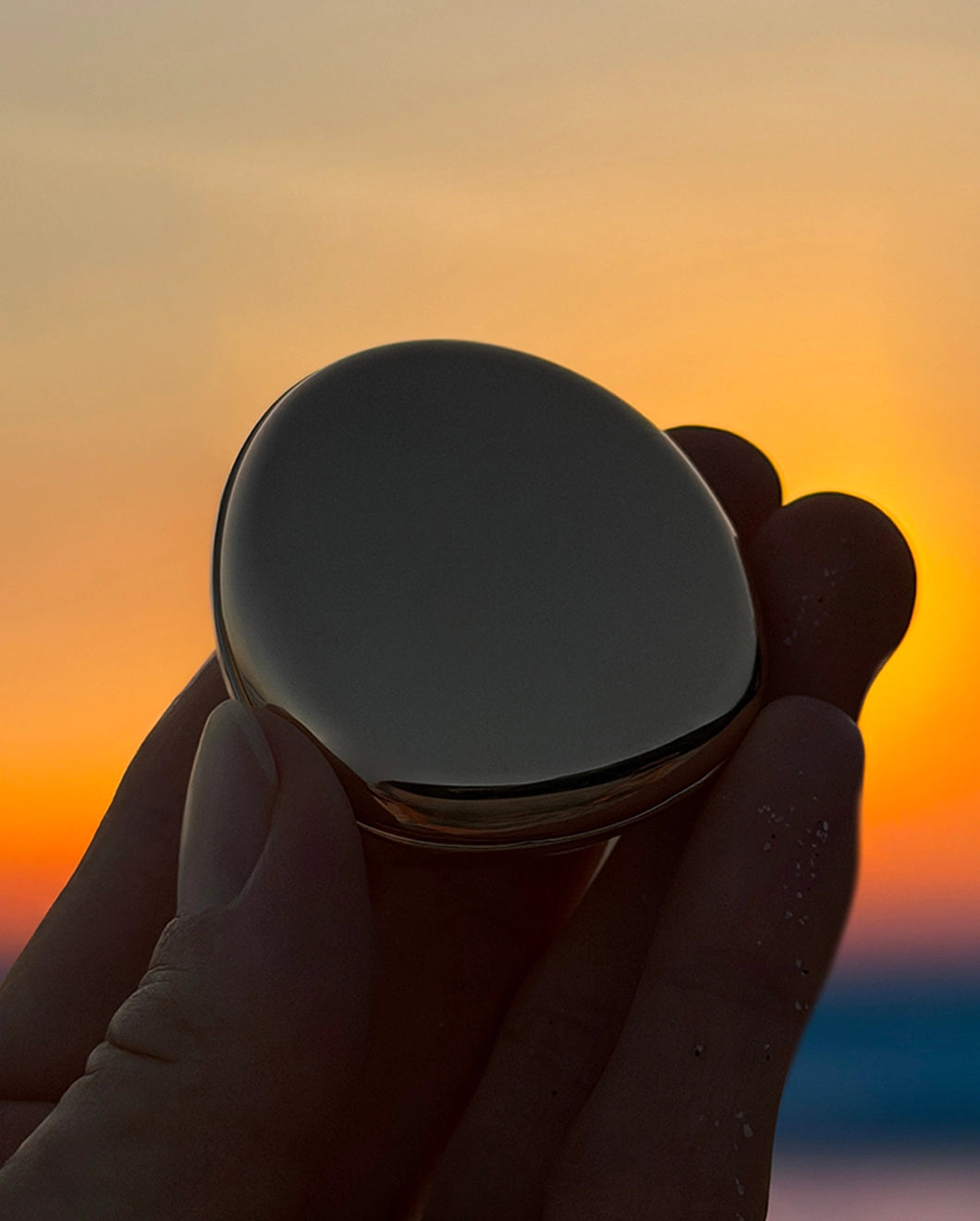 Close-up of Blu & Green's Juniper Dawn Solid Scent being held in front of a colorful sunrise.