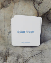 Load image into Gallery viewer, blu and green daily shampoo tablets in flat square off-white tin with a medium blue logo, multiple tins stacked on pale grey dry rocks, diffused sunlight. 
