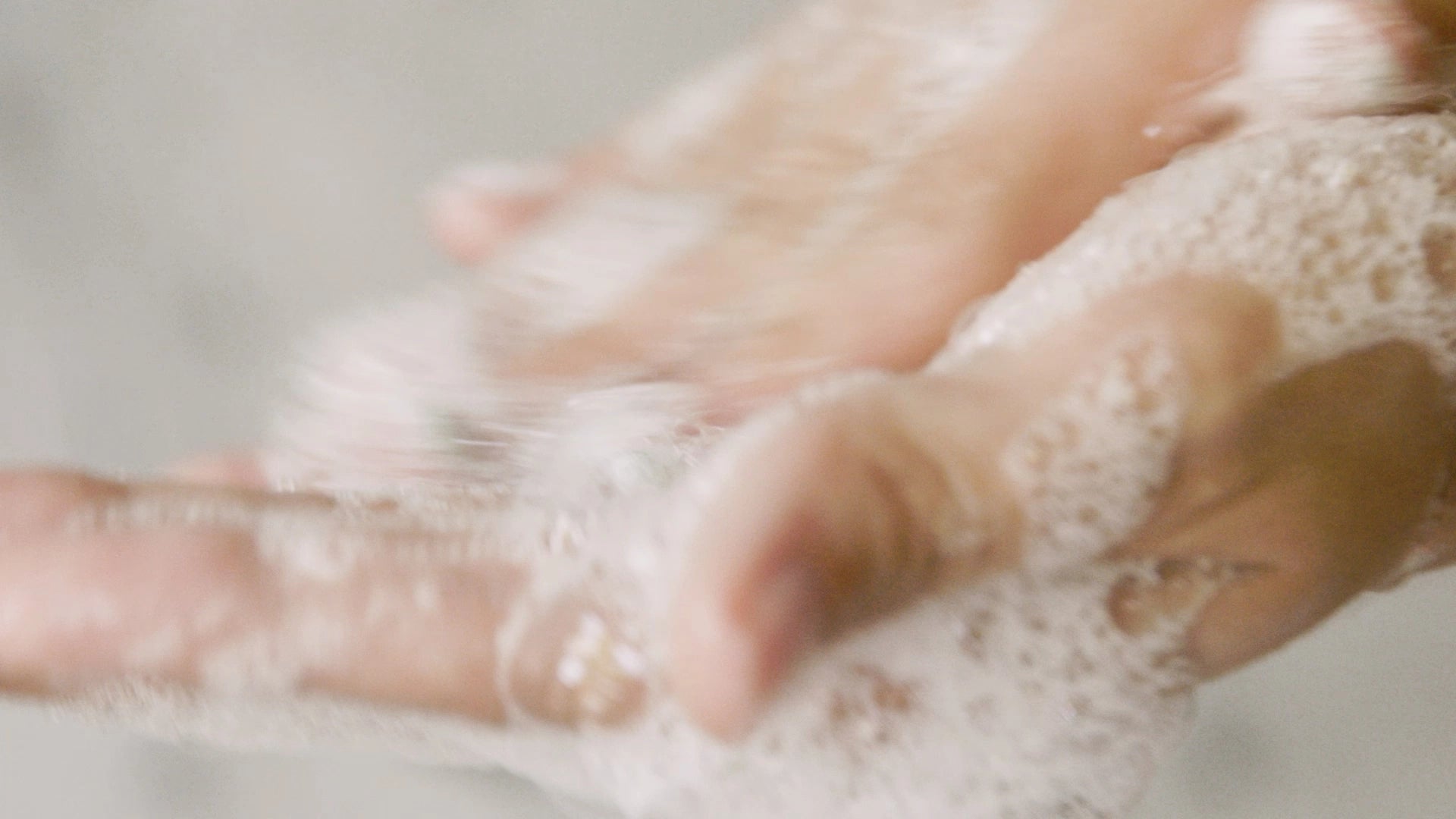 Close-up of hands with shampoo lather on a neutral background