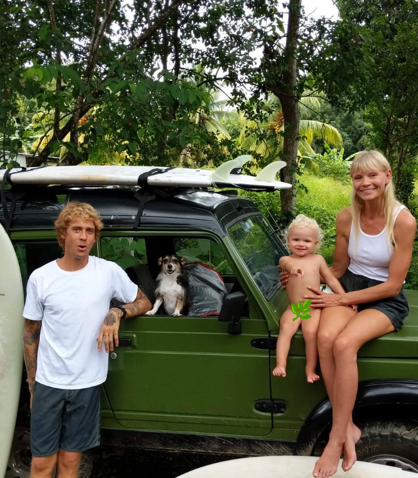 Blu & Green founders family portrait, with family standing and sitting on a green vehicle with surfboards, surrounded by tropical greenery, with a dog in the front seat.