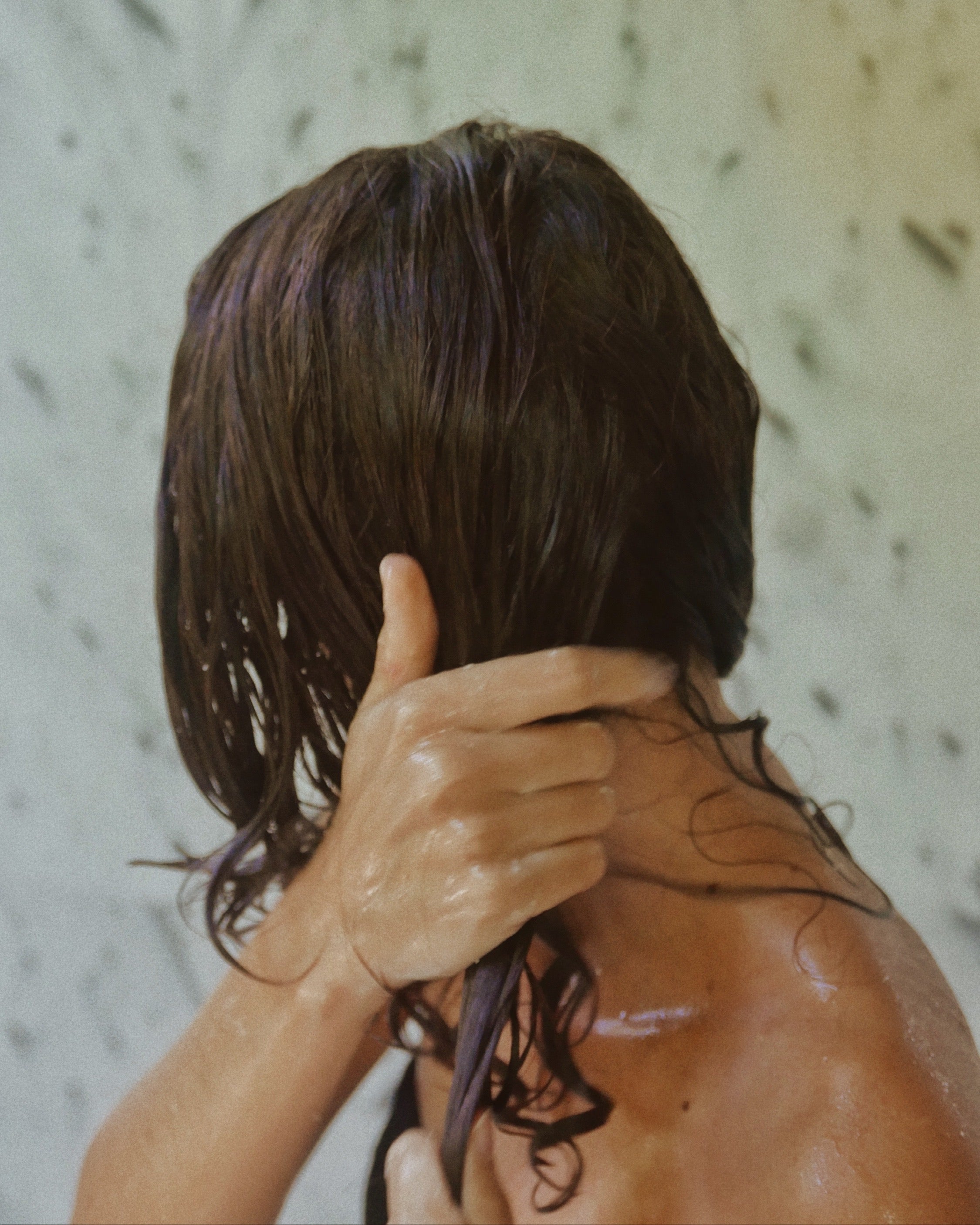 Back view of woman in shower applying Blu & Green Weekly Repair Mask to wet hair after cleansing.