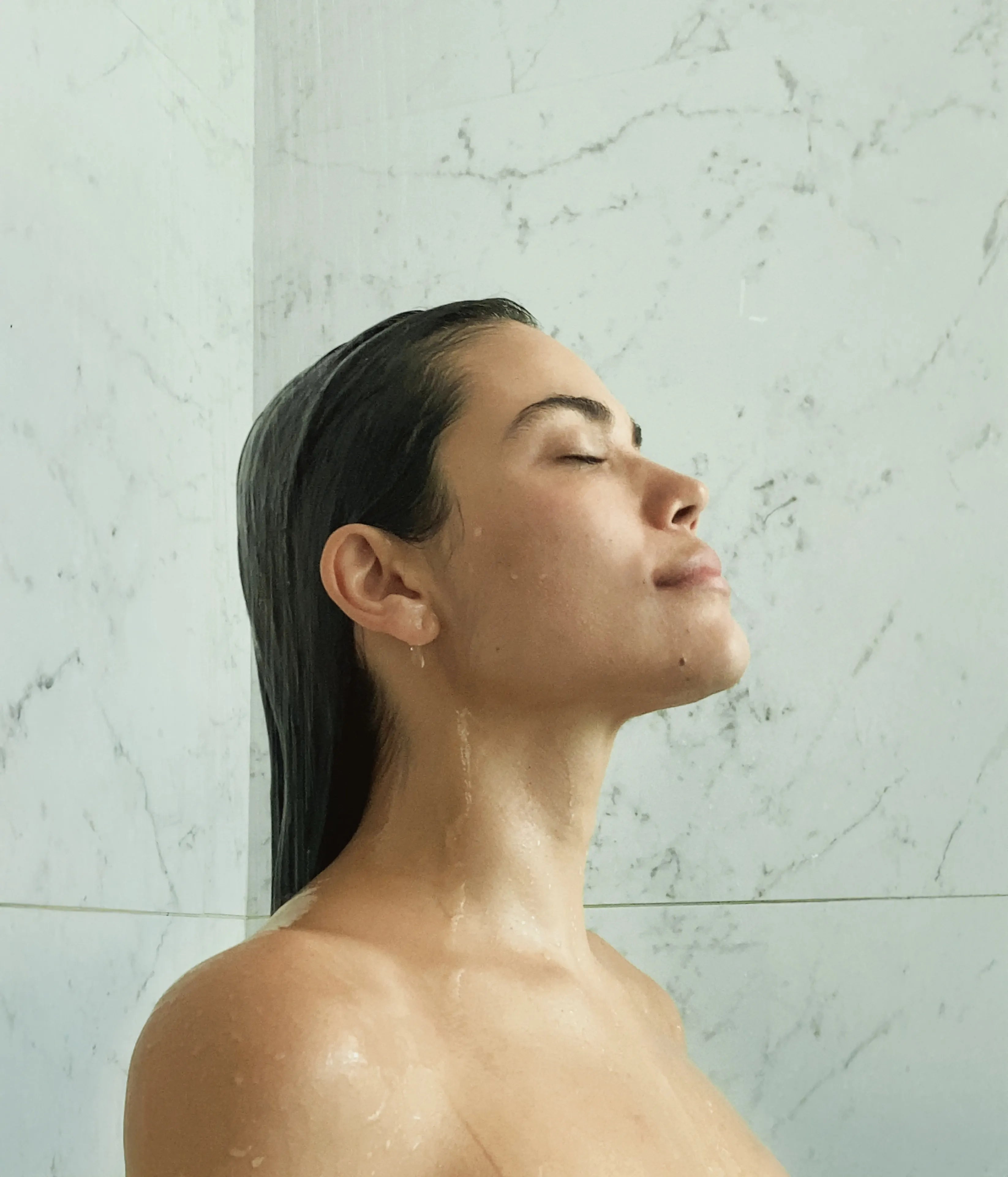 Woman with wet hair in a marble shower.