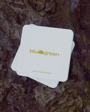 Load image into Gallery viewer, blu and green daily conditioner tablets off-white tin with a pale mustard green colored logo, multiple tins stacked on dark wet rocks, diffused sunlight. 
