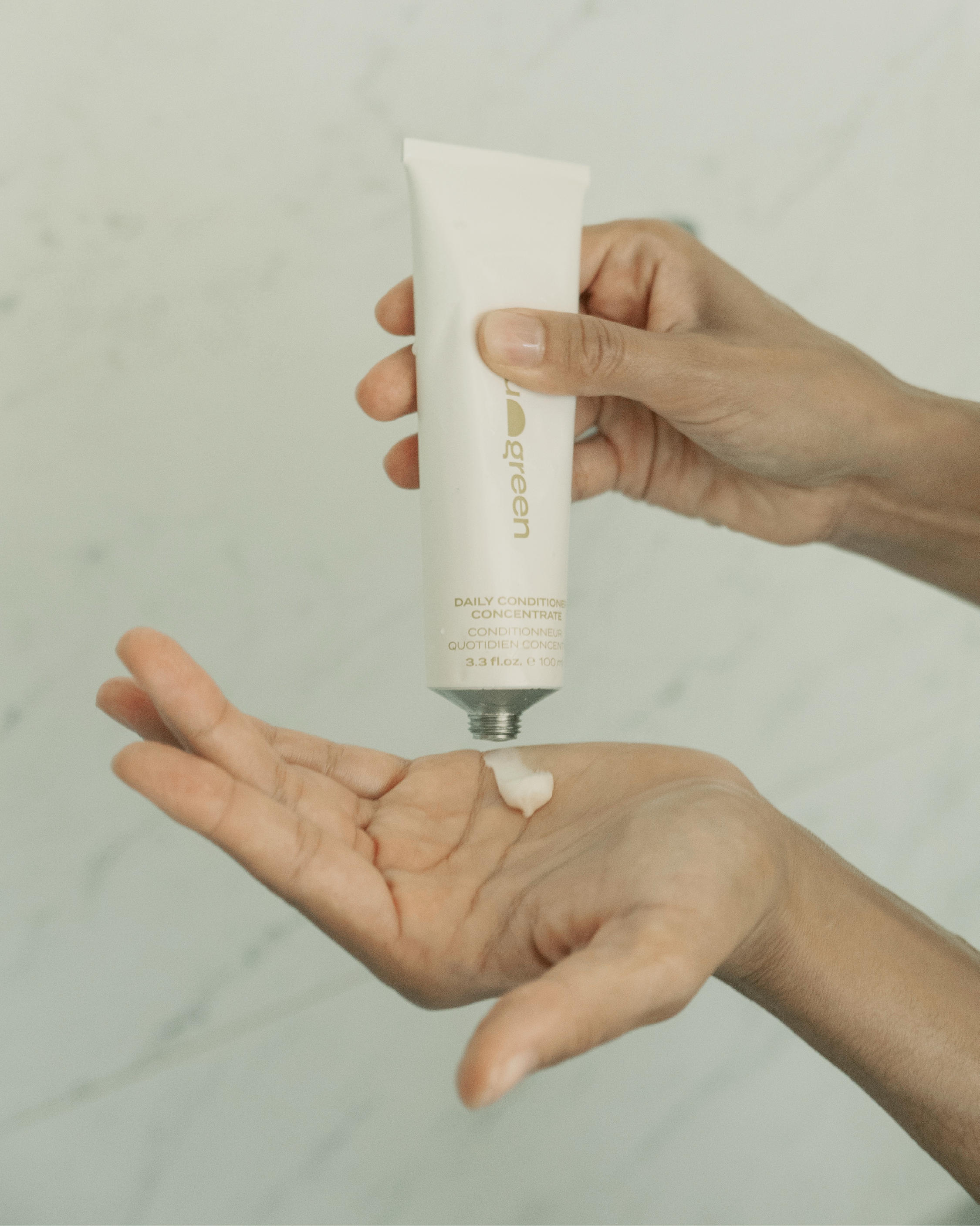 Blu & Green Daily Conditioner Concentrate being squeezed into palm in shower, showcasing the creamy texture.