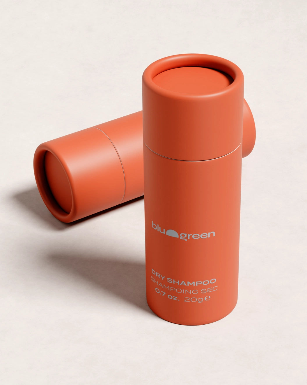 Blu & Green Dry Shampoo, 20g orange bottle standing upright with one lying flat behind, aerosol-free hair powder.