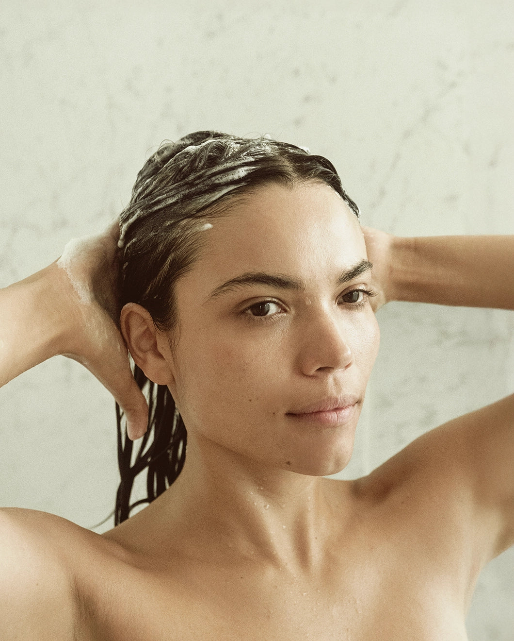 Woman in the shower lathering the Blu & Green Daily Shampoo Concentrate into her hair.