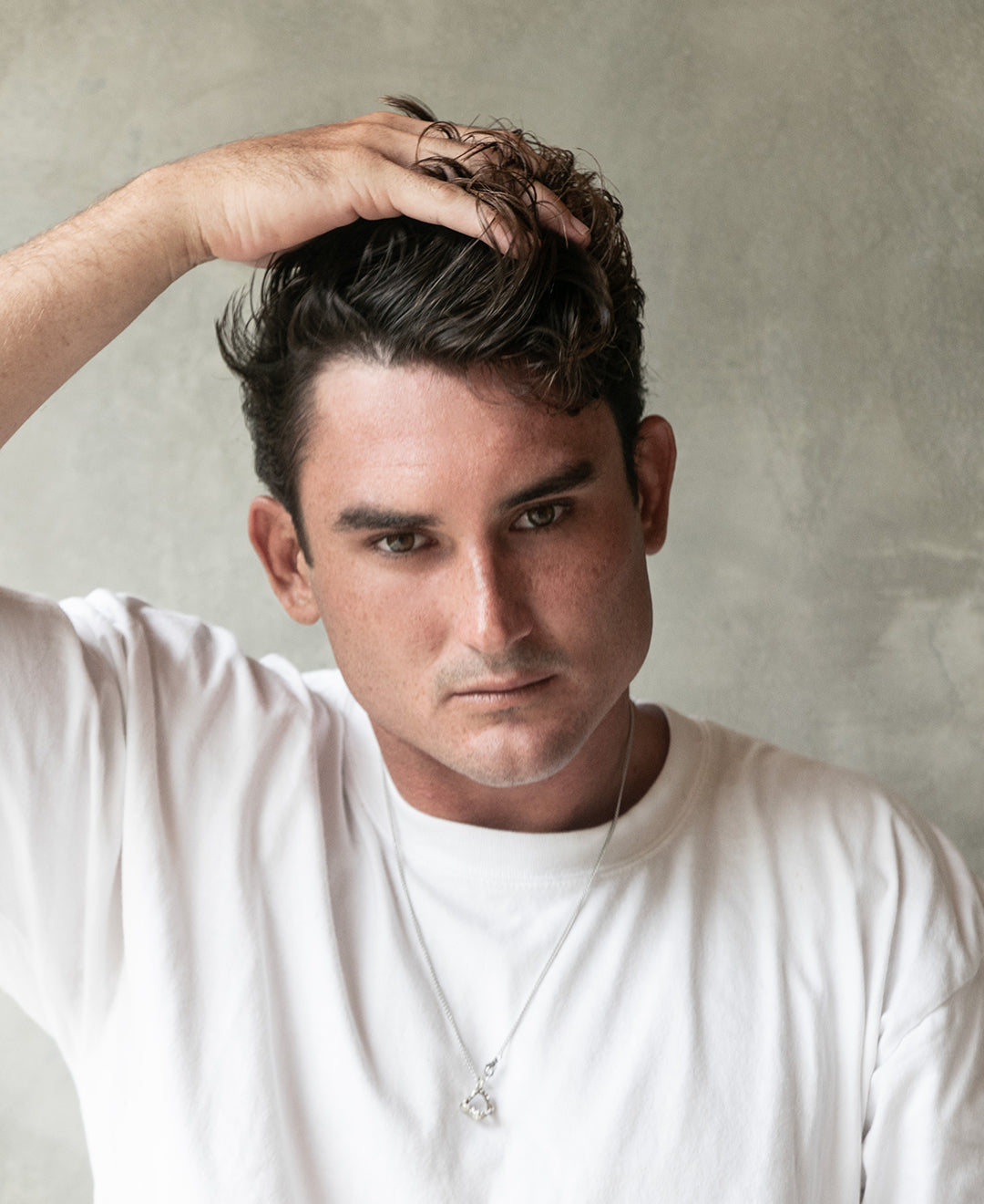 Man with short hair styled with Blu & Green Solid Oil, touching his hair with one hand.