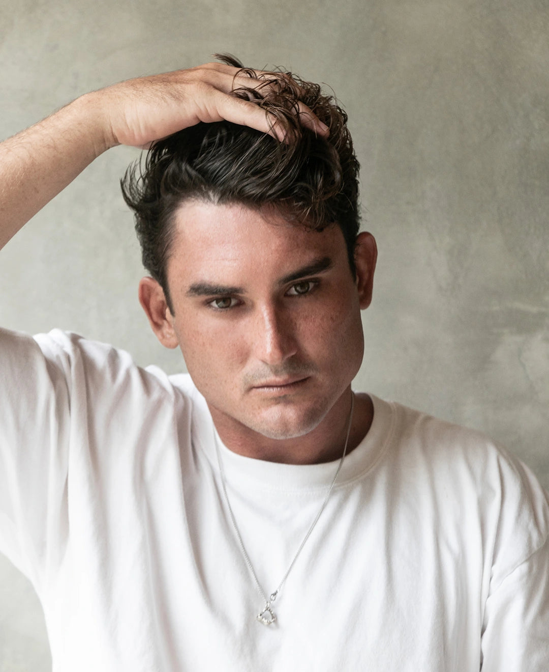 Man with short hair styled with Blu & Green Solid Oil, touching his hair with one hand.